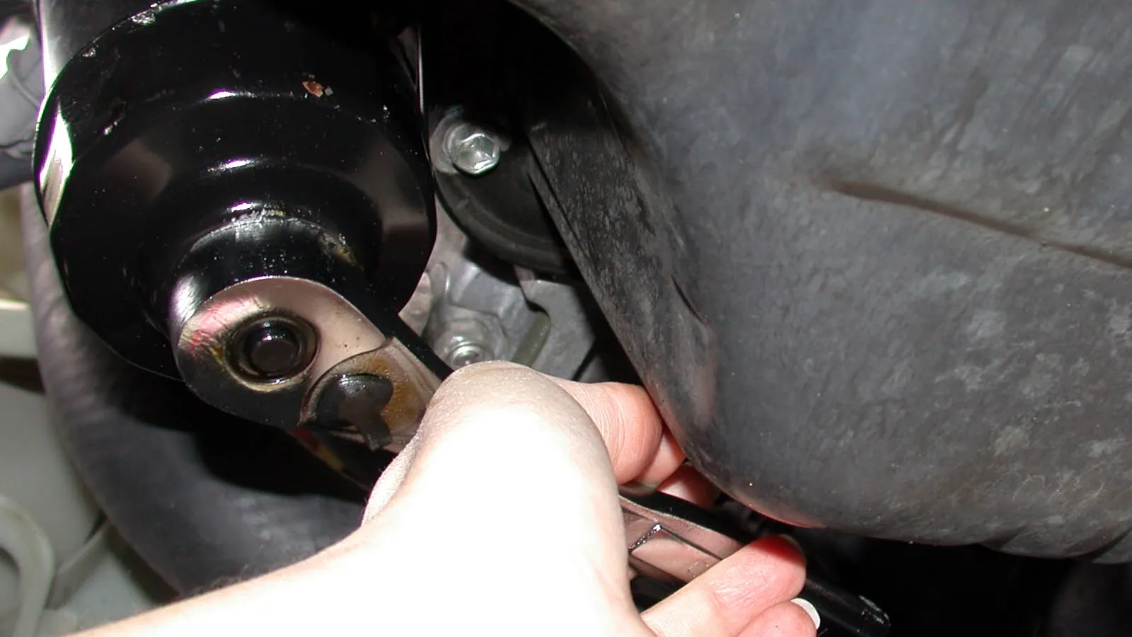 Person draining old engine oil on a ramp with the oil pan drain plug open